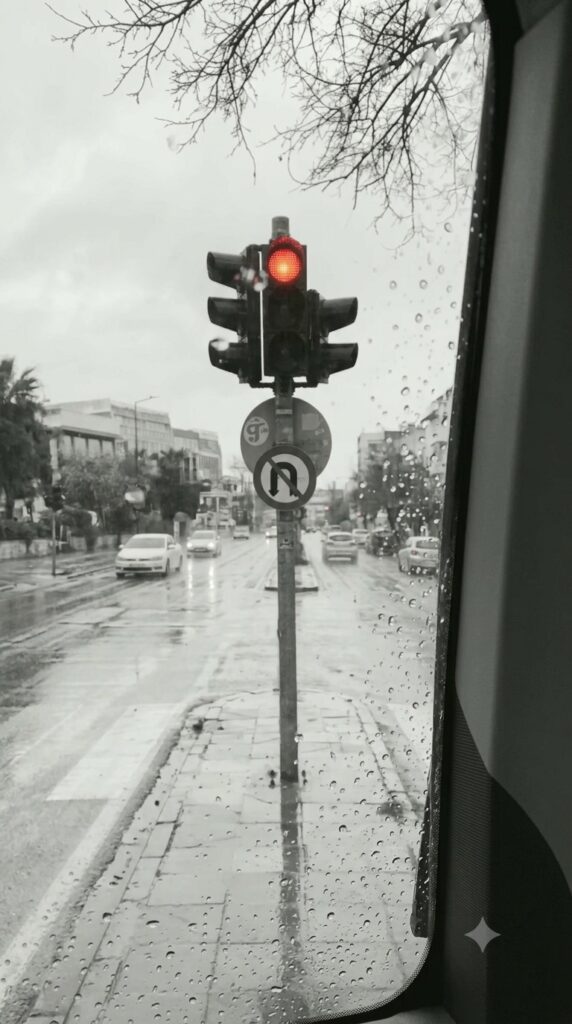 Κόκκινο φανάρι σε βροχερό δρόμο μέσα στη γκρι πόλη.