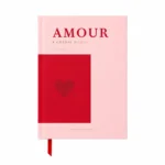 Ροζ σημειωματάριο A5 με σκληρό εξώφυλλο AMOUR & Cheesy Words της All The Ways To Say, κόκκινη καρδιά και κόκκινη κορδέλα σελιδοδείκτη.