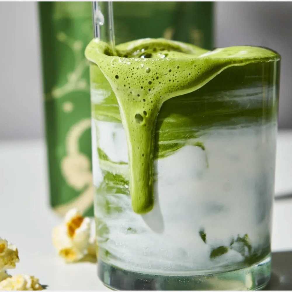 Matcha latte σε γυάλινο ποτήρι με γάλα και πλούσιο πράσινο αφρό.
